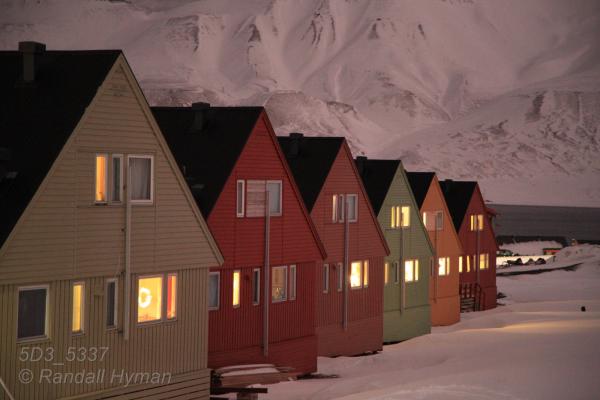 Colorful homes catch glow of rosy polar stratus clouds in the polar night of January in Longyearbyen, Svalbard, Norway.