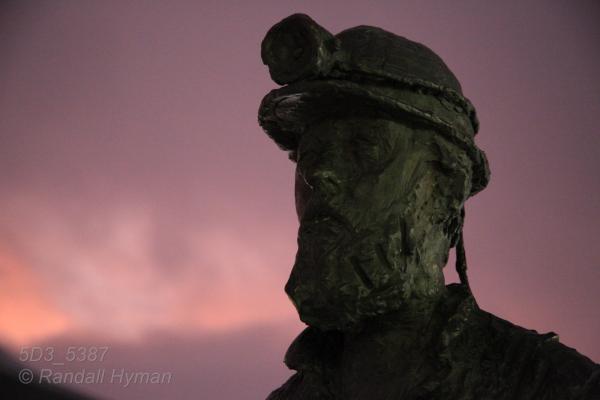 Bronze miner statue catches glow of rosy polar stratus clouds in the polar night of January in Longyearbyen, Svalbard, Norway.