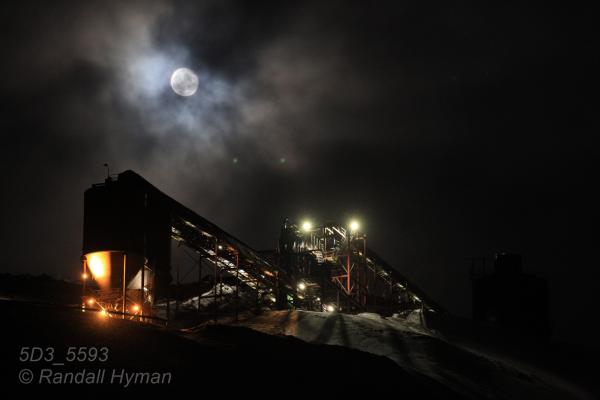 Storm clouds whisk across full moon above Mine 7 entrance in the polar night of January in Longyearbyen, Svalbard, Norway.