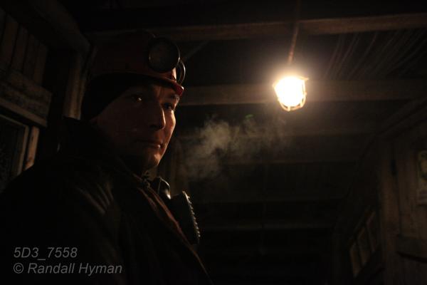 Coal miner pauses under lone electric bulb before turning on headlamp and going underground in Barentsburg, Svalbard, Norway.