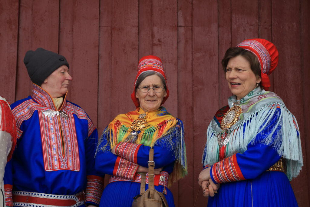 Three Sami women in traditional folk costumes, or gákti, pause outside main Lutheran church in town of Kautokeino, Finnmark after Easter morning services.