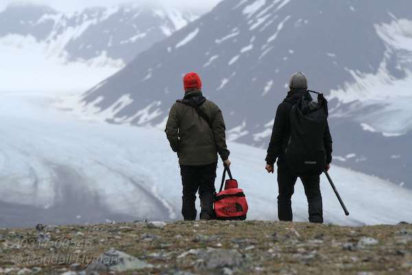 Glacier and mountains of Spitsbergen island greet biologists Borge Moe and Sveinn Are Hanssen (Norwegian Institute for Nature Research) as they hike across Storholmen island during field research on eider ducks in Kongsfjorden, Svalbard.