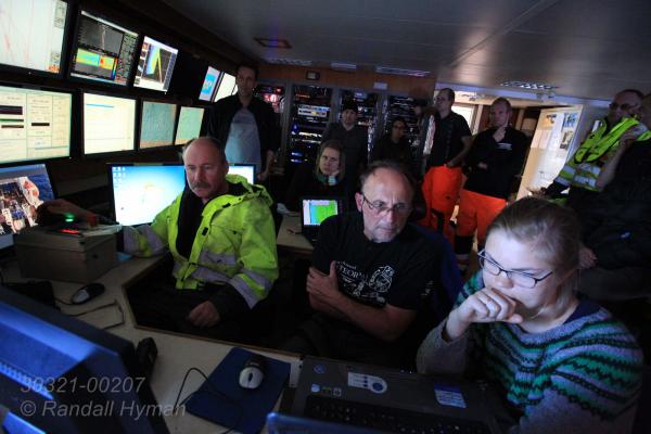 Scientists gather around computer and video monitors in instrument room aboard R/V Helmer Hanssen to monitor descent and release of unique seafloor lander at start of one-year CAGE mission tracking Arctic Ocean methane off west coast of Svalbard archipelago, Norway.