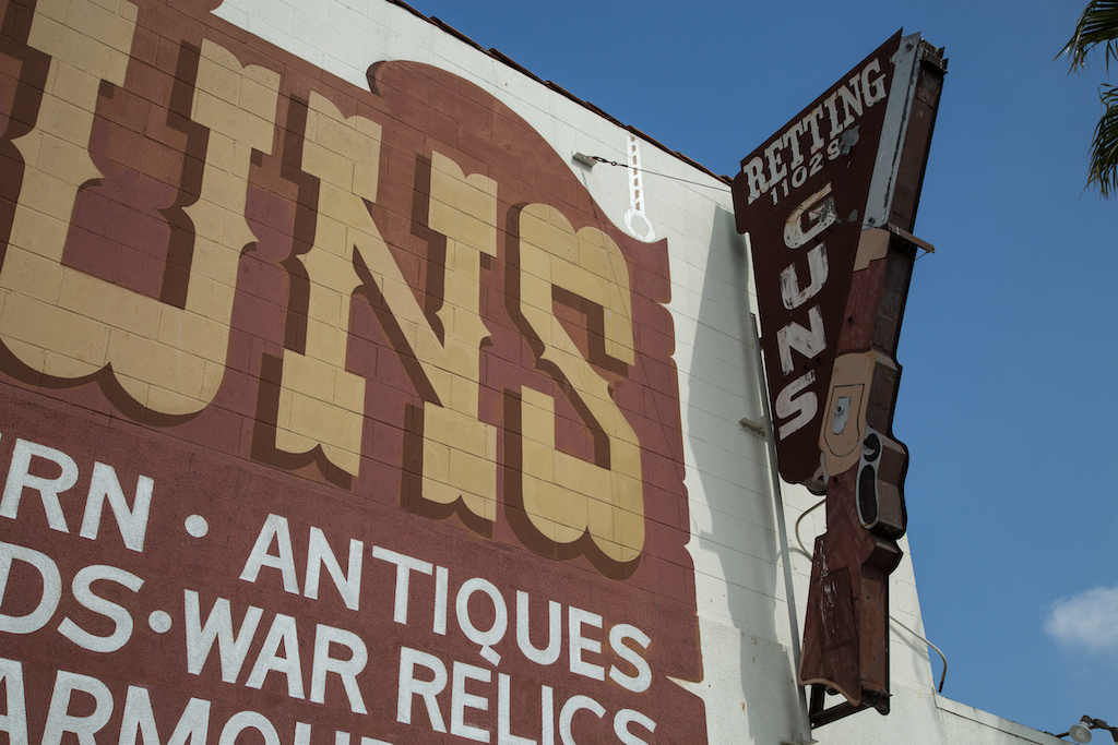 In Culver City, at 11029 Washington Boulevard, Martin B. Retting has a rifle painted on the side of the building, as well as fashioned on a blade sign. A large hand lettered sign advertises modern and antique guns, swords, war relics and armor.