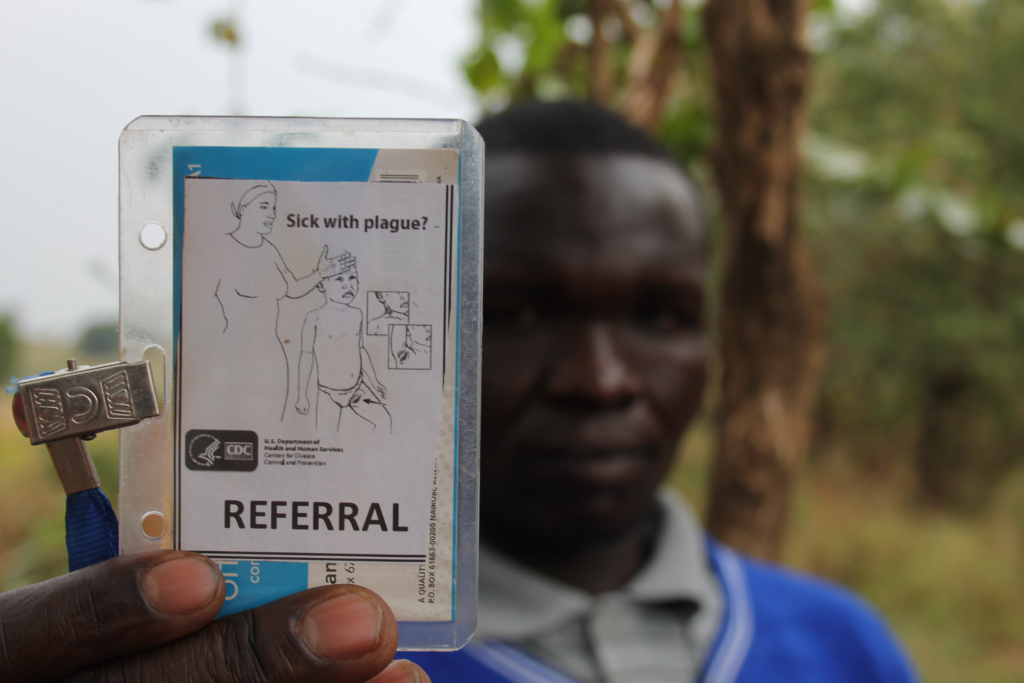 A traditional Ugandan healer holds a referral card, developed by the U.S. Centers for Disease Control, to give to villagers suspected of having plague. The card directs them to a local clinic that uses antibiotics, rather than prayer and herbs, to treat the symptoms of plague.