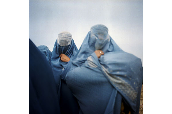 Women carry goods from the market under their burqas to the displacement camp where they live.