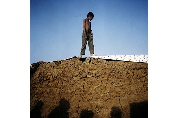 A boy helps his family pull a tarp over their mud walls that mark their new home after fleeing the violence in Kandahar.
