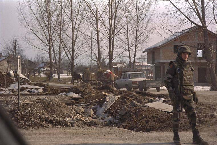 Serbs are in the background, in horse-drawn carts and cars, leaving Ilidza a day before the hand-over. A French NATO soldier stands guard at a road crossing.