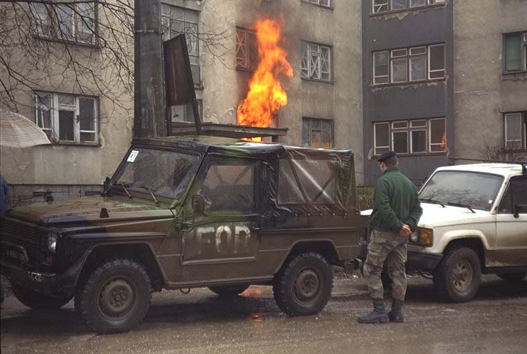 A NATO soldier stands next to his IFOR jeep as an apartment in Grbavica burns.
