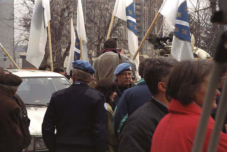 Blue-bereted members of the U.N. International Police Task Force stand on the Bridge of Brotherhood and Unity, which links government-held Sarajevo with Serb-held Grbavica. This had been no-man's land during the war. They are waiting, with a crowd of Bosnians, to cross over for a ceremony to hand over Serb suburbs to a Muslim-Croat federation. Robert Wasserman, the American who serves as deputy international police commissioner, faces front.