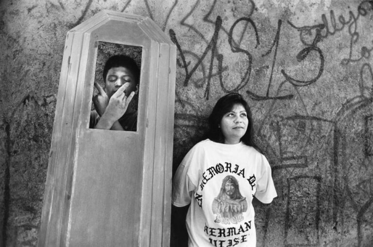 Sonia, a young Los Angeles girt, wears a memorial T-shirt from her brother Ulises’ gang funeral. A local Mara Salvatrucha gang member raises the lid of the coffin he was sanding to strike a pose of respect to the memory of his dead homeboy. Photo by APF Fellow Donna Decesare