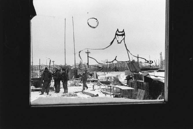 After a week of demonstrations in Grozny's central square, Russian soldiers begin to clear the debris and makeshift houses built by Chechens to protest the Russian occupation. The view is seen through a window which has the Chechen symbol, a wolf, painted on it.