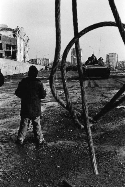 A young boy watches a Russian patrol rumbling down a destroyed street in downtown Grozny.
