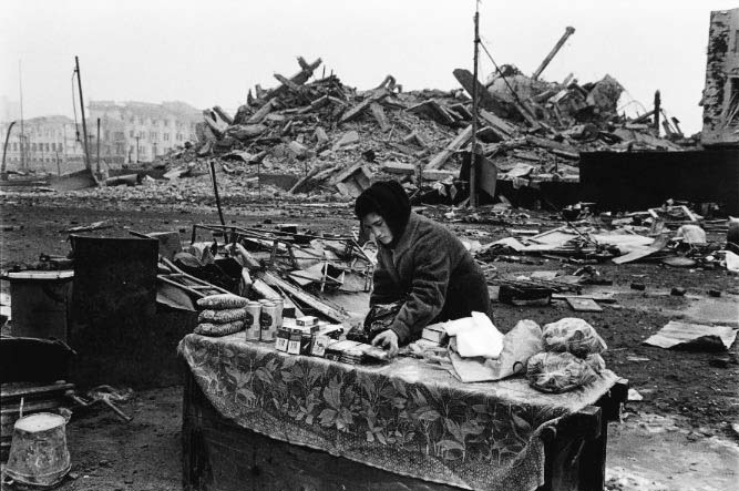 A young woman sets us shop in the center of Grozny. Behind her, the presidential palace is in ruins. Just days before, it was destroyed by three Russian blasts in order to deter Chechens from demonstrating there. Its destruction attempted to cripple morale as it was a symbol of the Chechan cause.