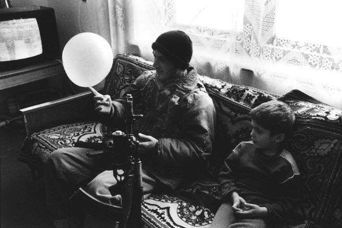 A Chechen rebel plays with his son's balloon while Russian news from Moscow issues Yeltsin propaganda on the war.