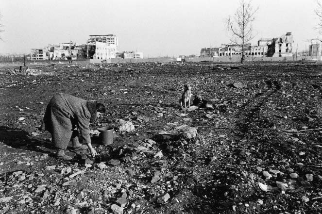 A woman gathers water from a tiny well in the center of Grozny, where buildings once stood. Her own home is only half-standing.