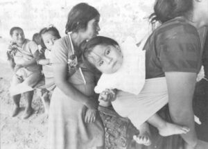 A child is carried by her mother, waiting in line for donated food at a refugee camp, La Gloria, in Chiapas, Mexico.