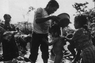 A finca worker washes his daughter in a river of mud. There were no bathing facilities at the finca and the drinking water supply was meager. Workers had. to bath and wash clothes in a low spot in the road where. a creek crossed The water drains from the chemical-laced cotton fields nearby.