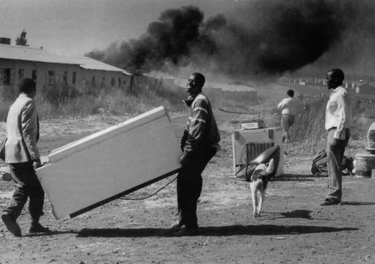 A Freezer is carried from the burning workers' hostel as Xhosa people looted and set fire to rooms that were accupied by Zulus. Fighting among black factions devastated the South African townships and is a huge issue for the Truth Commission.