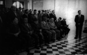 The aged members of the burial society sit in the Ceremonial Hall of the Jewish cemetery in Prague. Most of the 1,000 registered Jews in Prague are in their 70's and 80's. The chief of the cemetery, Arthur Radvanské, stands at right. He tended the bathrooms of the SS hospital in Auschwitz. He was ordered to massage Josef Mengel every Monday and Friday from 1942-1945 at Auchwitz.