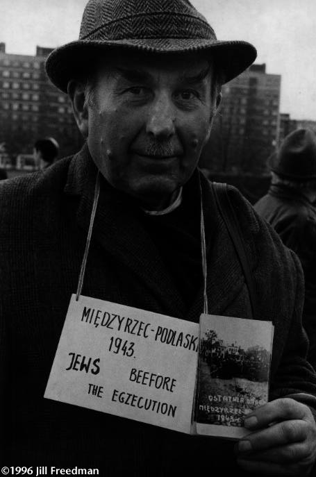 This Pole is at the Warsaw Ghetto Memorial, selling photos of Jews kneeling in a town center during World War II, waiting to be executed. He is trying to make money off the Jewish mourners who returned for the 50th anniversary of the Warsaw ghetto. Survivor Abraham Aviel, then 14, described a similar scene in the white Russian village of Radun. "We were brought to the marketplace in the middle of town. We were told to kneel, heads down. Of course we saw from the corner of our eyes the people who tried to run away were shot right there." The 3,400 Jews of Radun were taken to the Jewish cemetery and shot at specially prepared pits. More than 1,600 were women; more than 800 were children. Aviel noticed a group of Jews who dug the graves. Knowing that his brother was in that group, he was able to join them. His thought was always, 'One must survive - uberleben - and tell what happened.