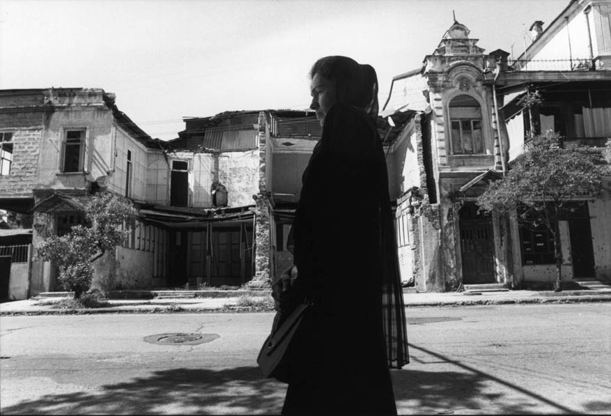 Against the backdrop of war ruins, a young widow — one of the thousands in Abkhazia — waits for a bus in Sukhumi, the capital of the self-proclaimed republic. With public transport scarce, the wait can stretch to an hour. Much of the city center, once lined with palms and oleander, now lies in rubble. Although the fighting ended four years ago, thanks to the post-war economic free-fall, few of the many ruined buildings have been restored.