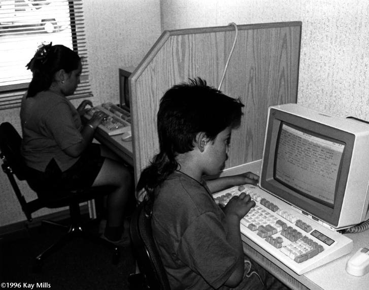 Allan Espinoza, front, works on his reading at a literacy van computer. Anthony Butera, a literacy specialist who drives the van to migrant camps in central California, is seeking an electronic encyclopedia to allow students to complete school reports.