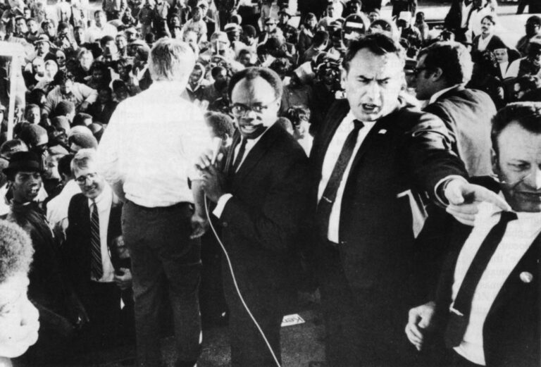 Robert F. Kennedy, his back turned, addressed a hostile crowd in May 1968 in Oakland while running for president in the California primary. The photograph was taken a week before Kennedy was killed in Los Angeles. To Kennedy's right is WIllie Brown who had just introduced Kennedy. Rep. Phillip Burton, is next to Brown with his arm outstreatched across the face of Assembly Speaker Jesse Unruh. A night earlier, Kennedy met with black militants in Oakland. When Brown tried to calm the crowd, he was heckled. Photo courtesy Bancroft Library, University of California, Berkeley.