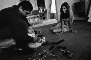 Chivo, an East Los Angeles gang member, teaches his daughter how to hold a 32-caliber pistol. Her mother, Yvonne, looks on.