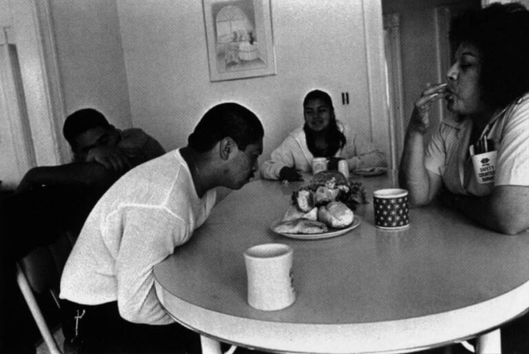 Chivo sits at the breakfast table with his mother (right) telling him he better get a job. His sister and friend, Boxer look on. His mother, a bus driver, then left for work.