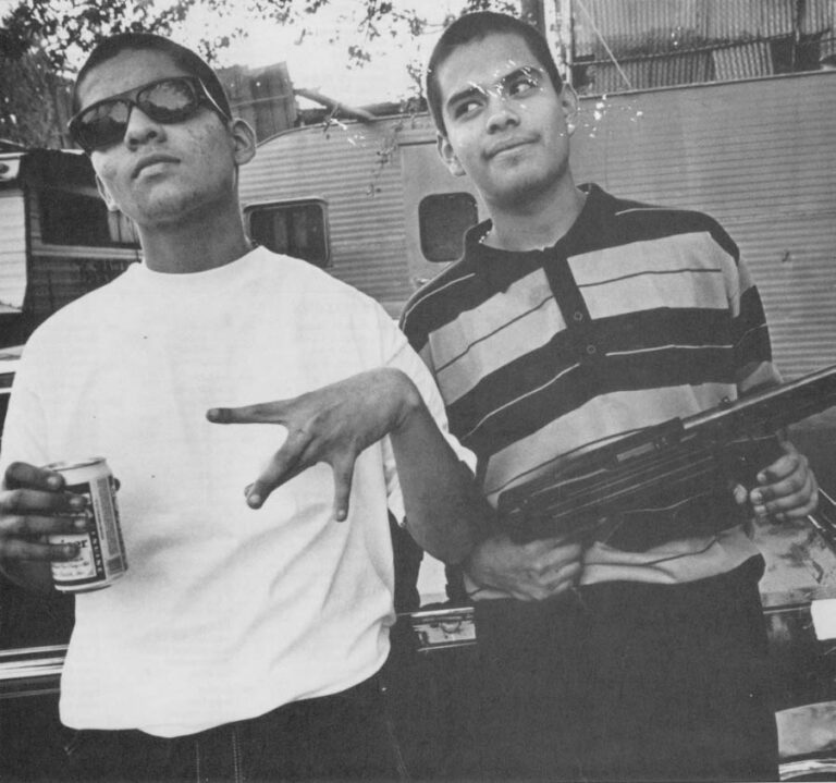 Porky, 16, right, and Jaime, of the Marianna Maravilla Diablos, an Easl Los Angeles gang, hold his machine gun in front of a car that Porky was shot in. "I love the barrio more than I was loved," Porky relates.