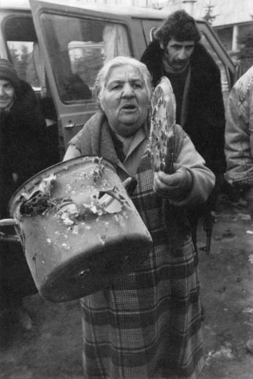 A Stepanakert woman shouts in anger over a rocket attack, displaying a cook pot shredded by shrapnel from a shell that landed in her home.
