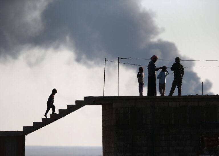 Residents of Al-Hawl, in northeastern Syria, speak with a Kurdish soldier while an oil well burns in the distance. Getty Images