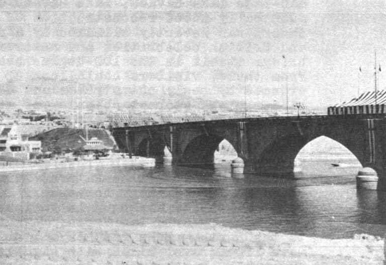 The reconstructed London Bridge spans a man-made channel at Lake Havasu City. To left of bridge is construction of replica London street, backdropped by grass trucked into this otherwise barren desert wasteland.