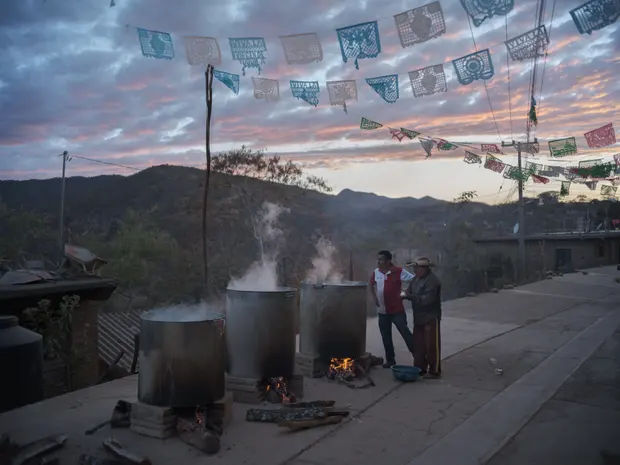 Smoke billows from a pot of pozole cooking over a wood fire.