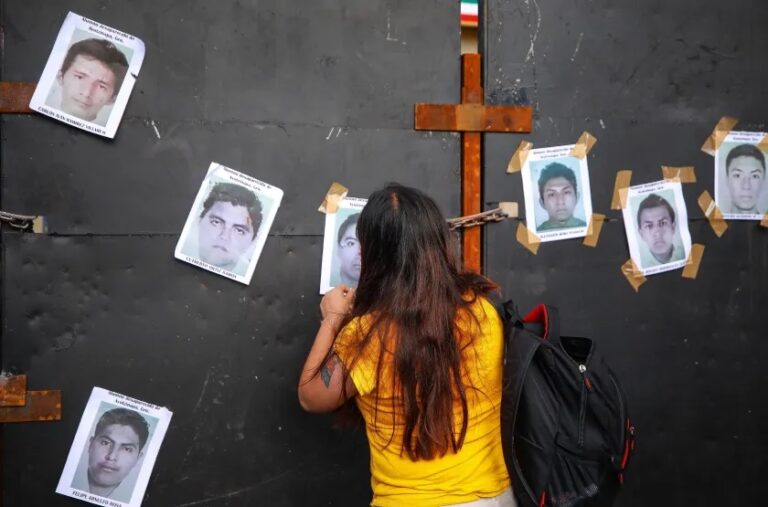 A woman puts photos of missing students on a wall on Sept. 26, 2022 outside the Palacio Nacional in Mexico City to commemorate the eighth anniversary of their disappearance. | Getty Images