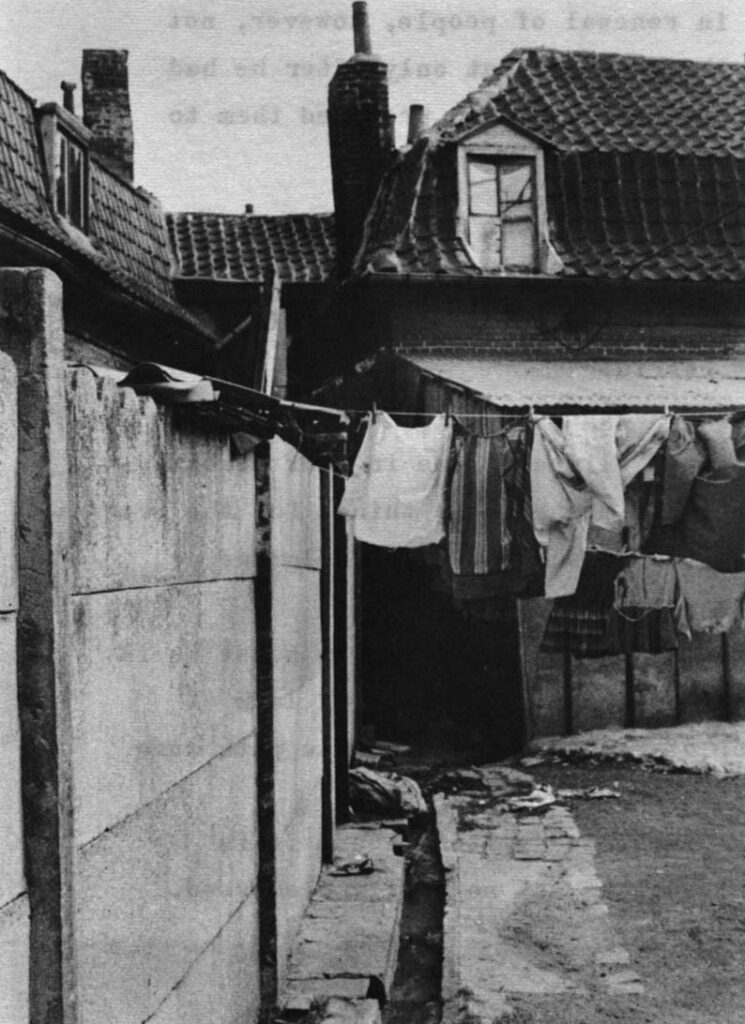 Courée scenes. The drain at top is the only sewer for the houses, which have no plumbing. The dark place under the clothes is the entrance to the couree. Most courees are entered by such dark tunnels through the houses facing the street. The word courée is derived from courette or small courtyard. To the bottom is the only water and the only toilet for 25 families. The tap, somewhat hard to see, is to the left of the outhouse door.