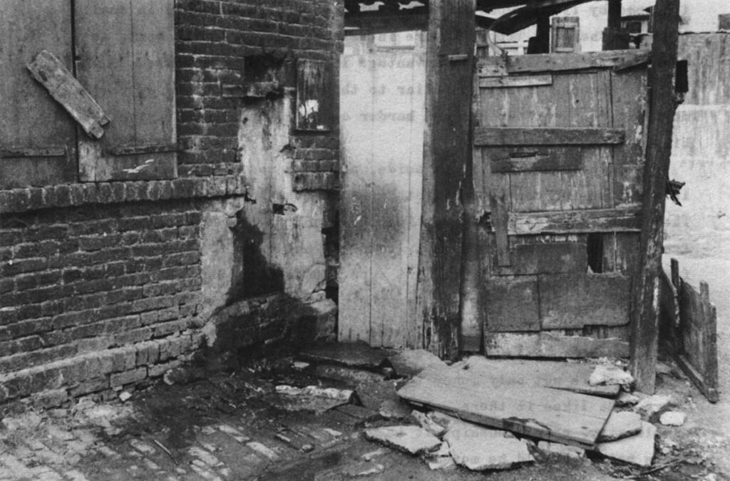 Courée scenes. The drain at top is the only sewer for the houses, which have no plumbing. The dark place under the clothes is the entrance to the couree. Most courees are entered by such dark tunnels through the houses facing the street. The word courée is derived from courette or small courtyard. To the bottom is the only water and the only toilet for 25 families. The tap, somewhat hard to see, is to the left of the outhouse door.